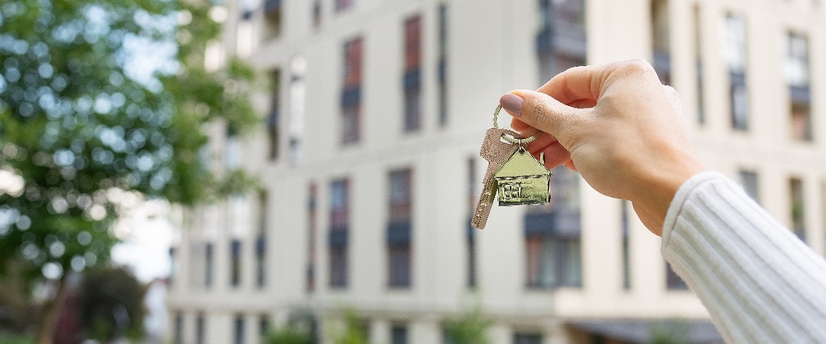 Hand holding keys on the background of a new building, construction concept. Buying real estate, housing, apartments.